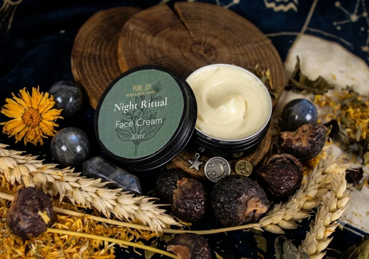 An open jar of Pure Joy Night Ritual face cream sits on wooden coasters surrounded by natural decor like wheat stalks, soap nuts, star charms, and crystals.